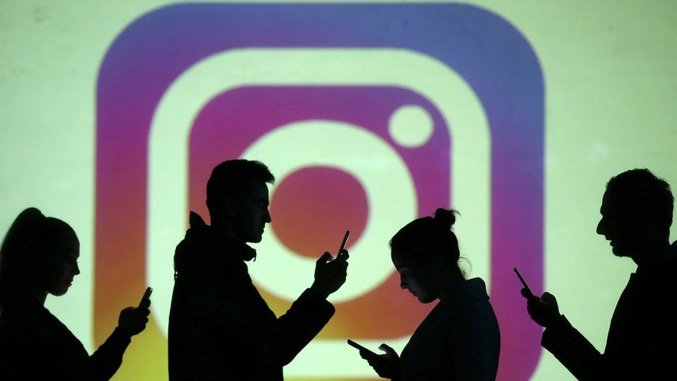 Silhouettes of mobile users are seen next to a screen projection of Instagram logo in this picture illustration taken March 28, 2018.