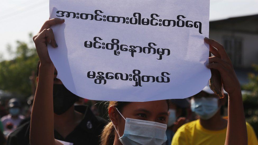 A demonstrator holds a placard with the words "Be Strong Mindat. There is a Mandalay behind you"