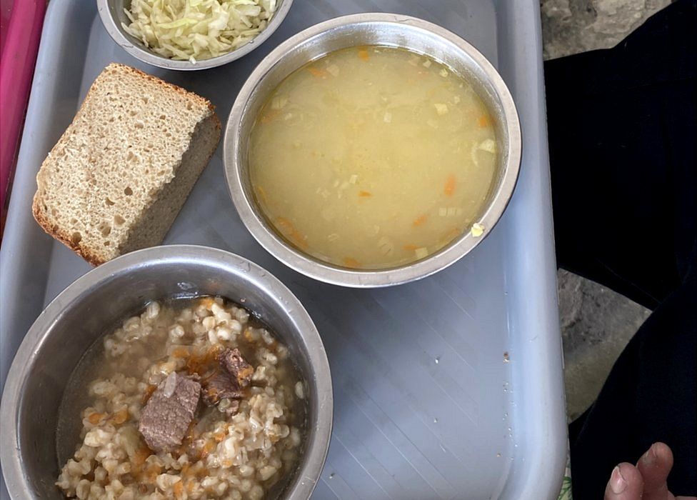 Die Gefangenen essen ein Mittagessen aus Brot, Maissuppe und einer Schüssel Gerste mit Fleisch