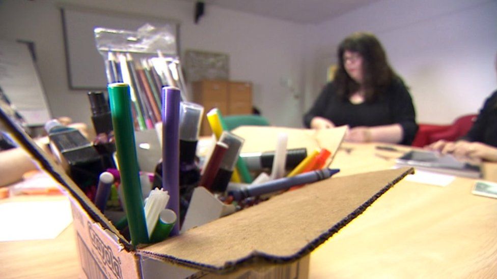 A box of coloured pens with a woman blurred in the background