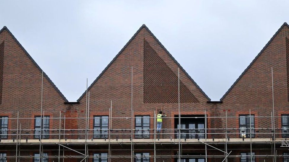 A worker stands on scaffolding to work outside a newly built residential property at a Barratt construction site for new houses and homes near Aylesbury, England, on 27 July 2023.