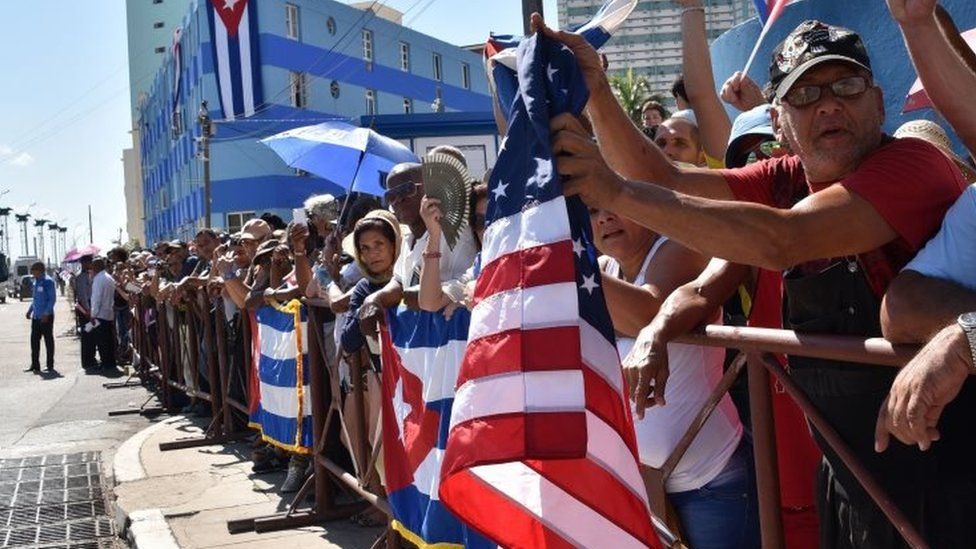 Кубинцы держат флаги США и Кубы у здания посольства США, когда над ним поднимается флаг США в Гаване 14 августа 2015 года во время визита госсекретаря США Джона Керри