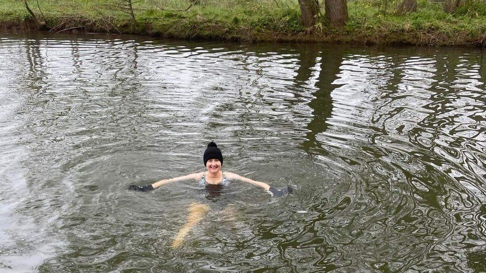 Woman in woolly hat swimming in river