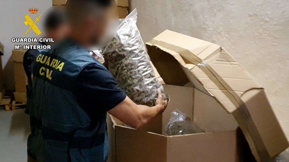 A police officer moves a bag of cannabis following a raid
