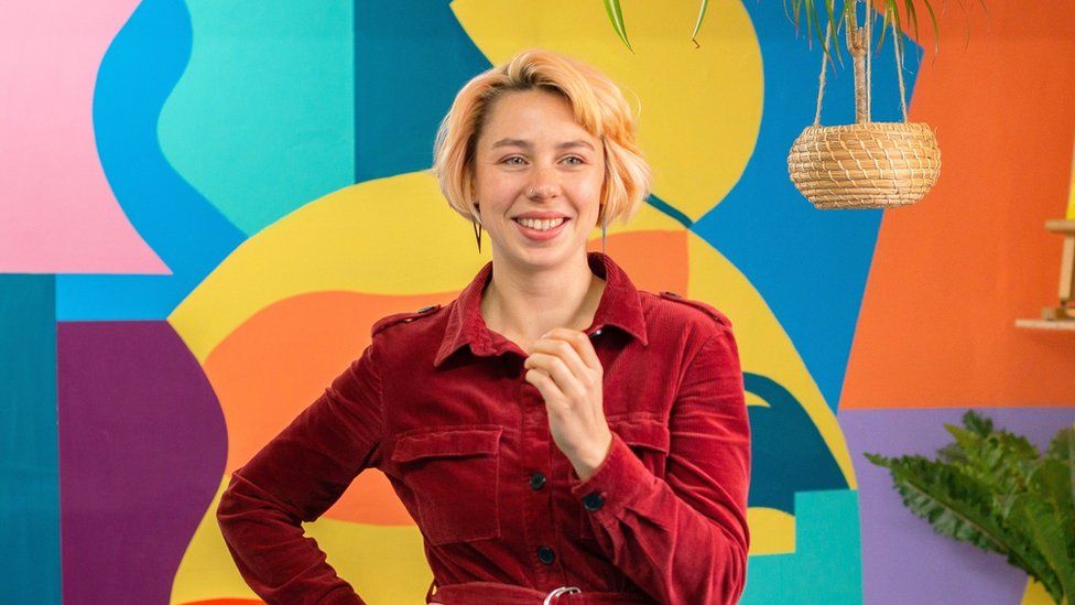 A woman wearing a red long sleeved top in front of a colourful background
