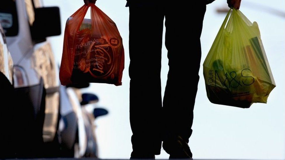 A man carries his shopping in plastic bags