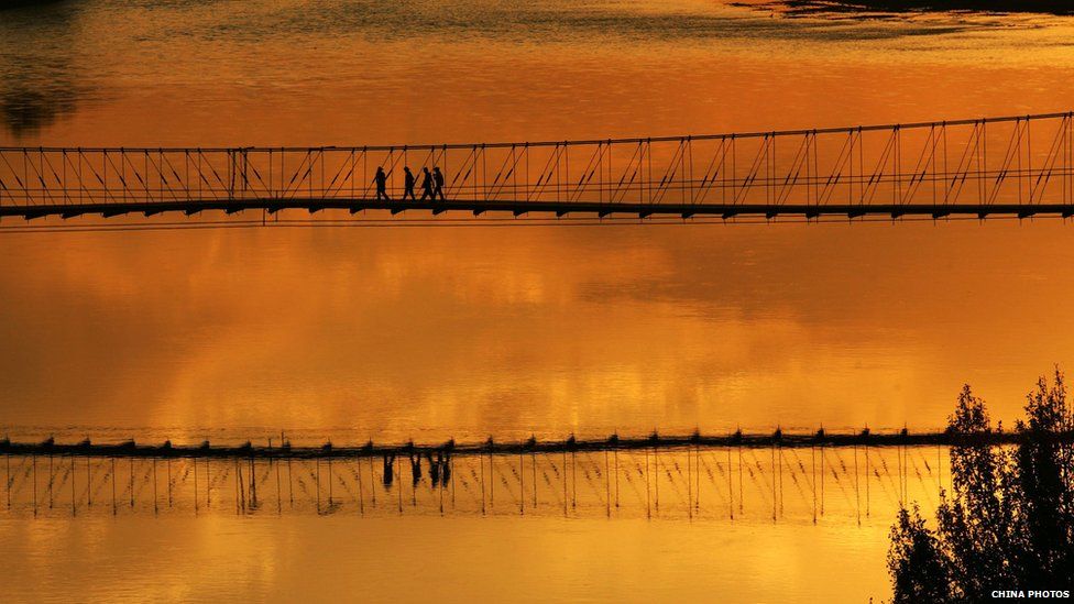 Tourists walk on a hanging bridge above the Ertix River to view the sunset at the Wucai Shoal, or Colorful Shoal, a typical example of lava landform on 13 September 2007 in Buerjin County of Xinjiang Uygur Autonomous Region, China.