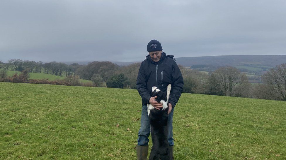 Russell Ashford stands in a field stroking his dog