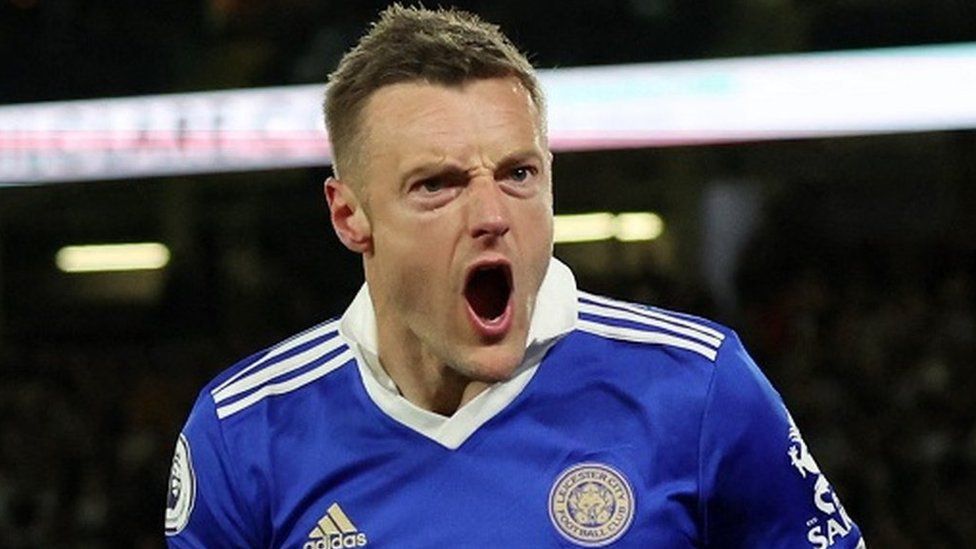 Jamie Vardy celebrating scoring a goal for Leicester. He has his mouth open as if he is shouting or roaring passionately. He's wearing a blue Leicester City home football kit and has short, brunette hair.