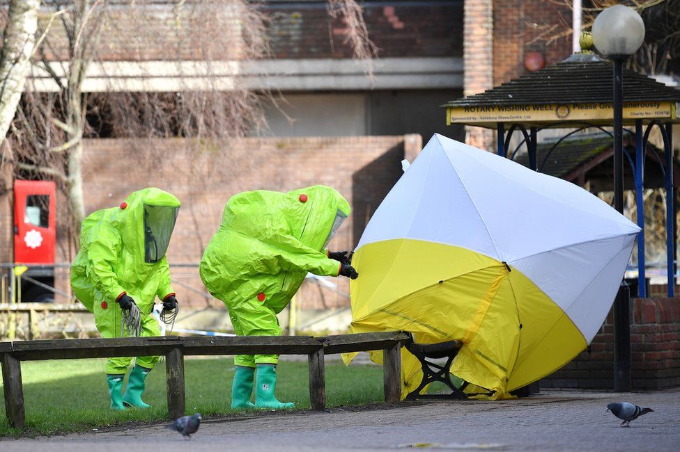 Members of the emergency services in green biohazard encapsulated suits fix the tent a bench