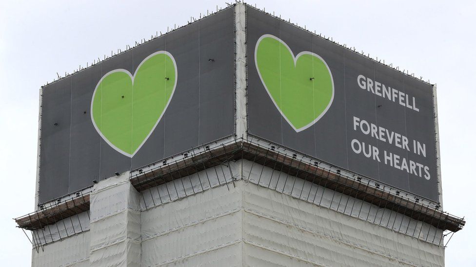 File image of the top of Grenfell tower covered in plastic and a banner reading 'Grenfell: forever in our hearts'