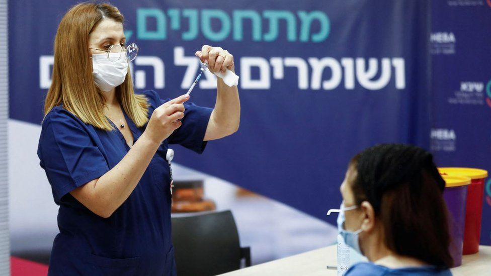 Israeli nurse preparing a Covid-19 vaccine while woman waits