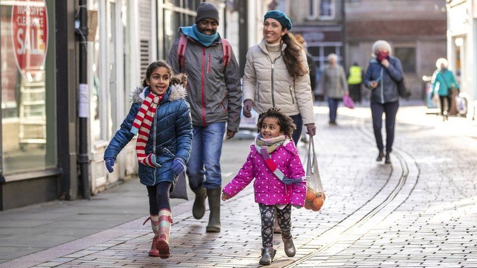 A family with two children walks down a high street wearing winter clothes