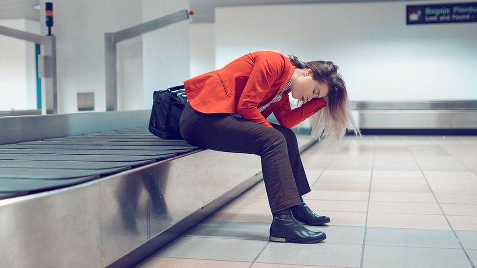 Woman with head in hands sitting on baggage carousel