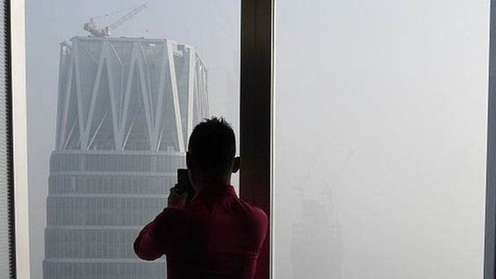 A man takes photos of buildings on a polluted day in Beijing