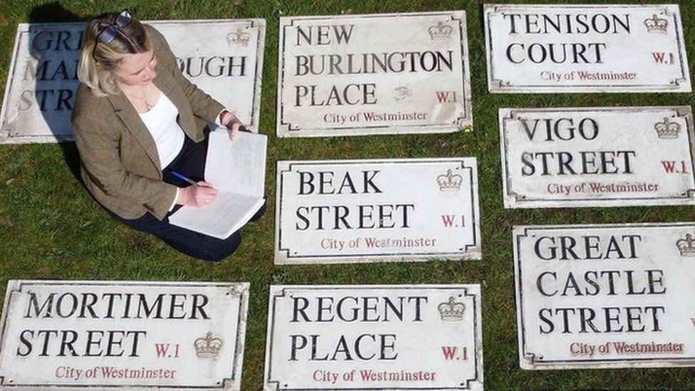 Woman sits with old London street signs