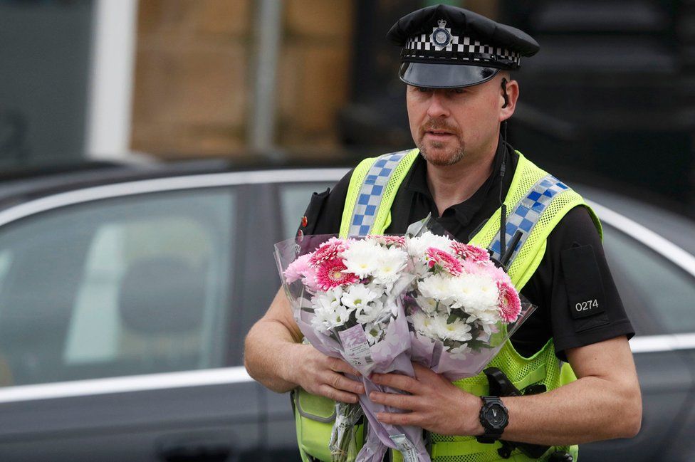 A police officer carries floral tributes