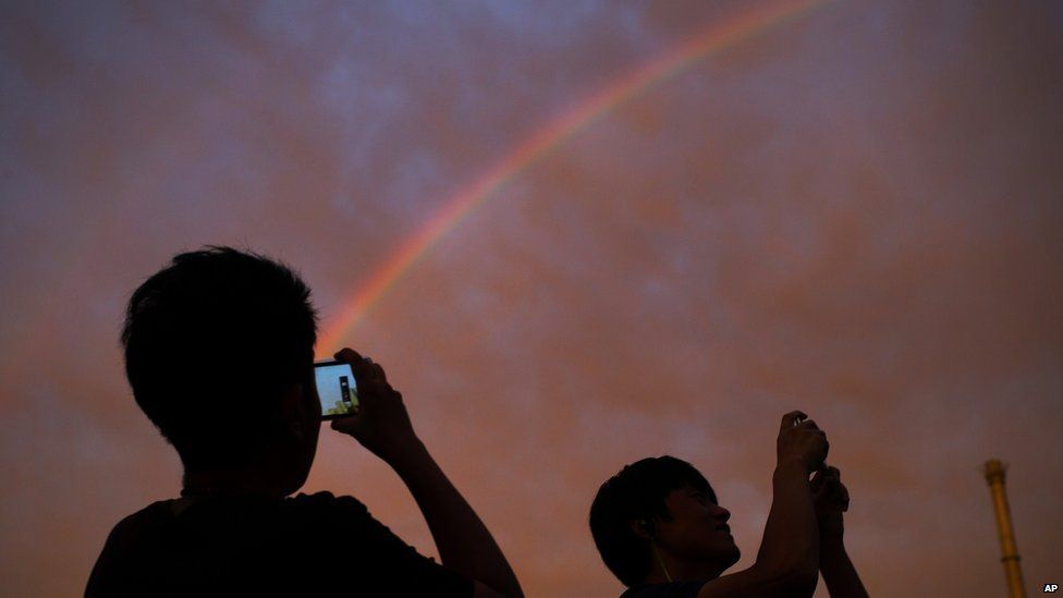 Passersby take photos of a rainbow at sunset in Beijing on Monday, 3 August, 2015