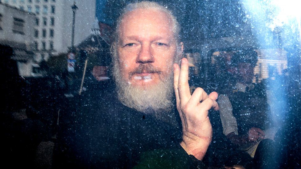 Julian Assange gestures to the media from a police vehicle on his arrival at Westminster Magistrates court on 11 April 2019