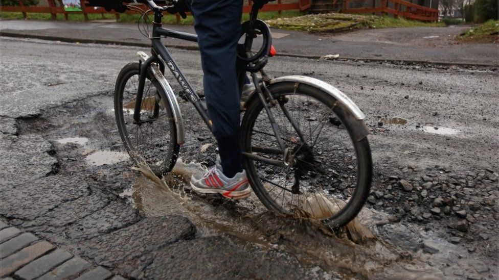 A cyclist rides through a pothole