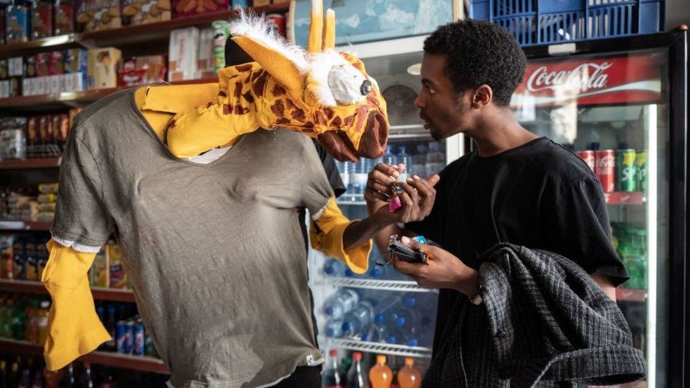 Human sized toy giraffe standing in a shop next to a man in Kigali, Rwanda - Friday 22 July 2022