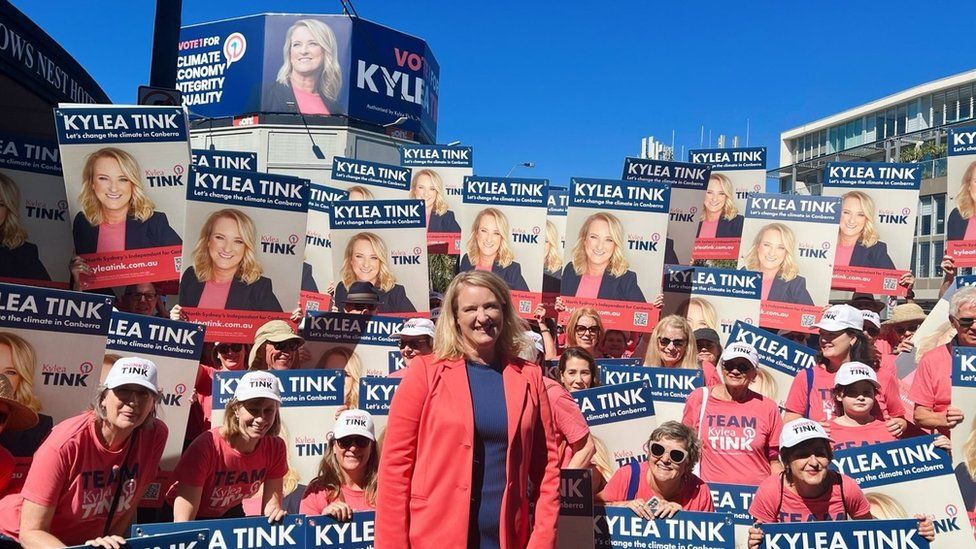 Независимый кандидат от Северного Сиднея Кайлеа Тинк на фото со сторонниками, держащими плакаты перед рекламным щитом, призывающим избирателей голосовать за нее.