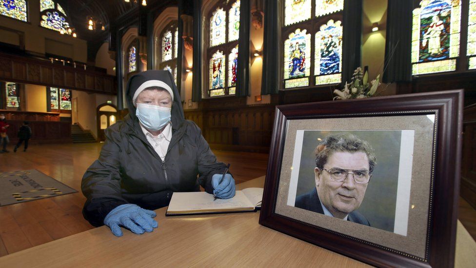 A nun wearing PPE signs the book of condolence at Derry's Guildhall