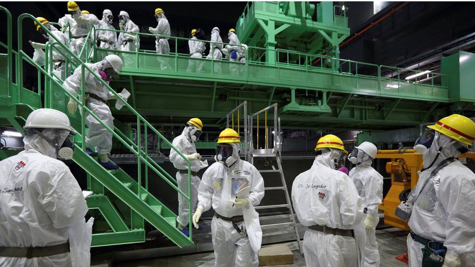 Members of the media and Tepco employees wearing protective suits and masks, near a fuel handling machine on the spent fuel pool inside the Number Four reactor building in the Fukushima Daiichi nuclear power plant, 7 November 2013.