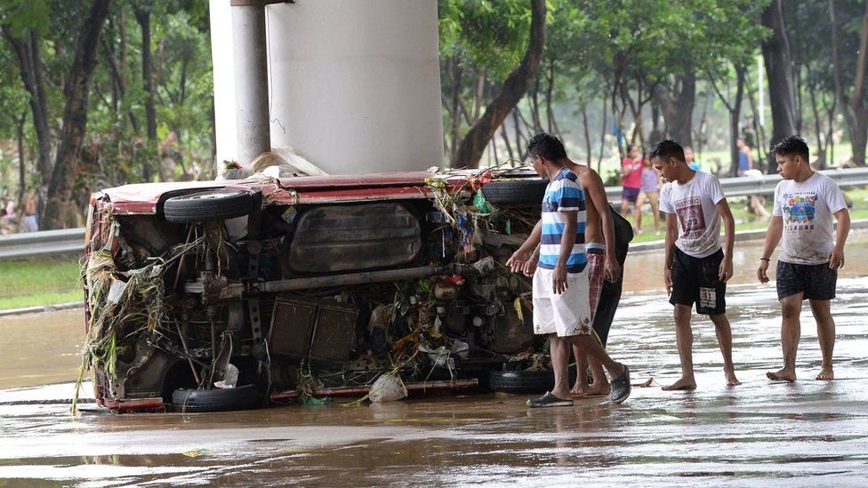 Manila residents walk past a washed up vehicle