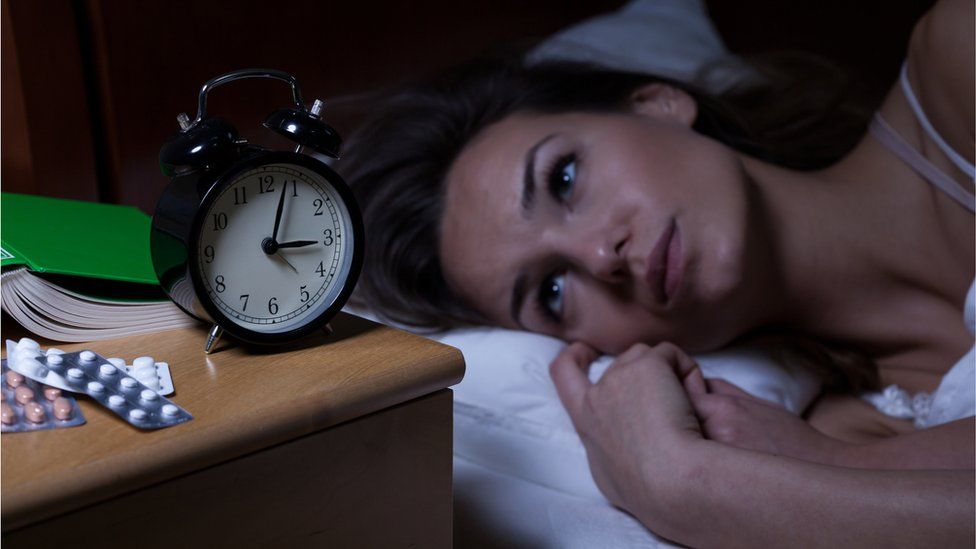 A woman struggling to sleep, looking at her alarm clock