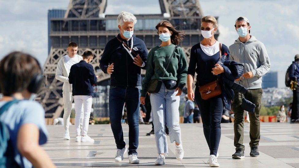 People wear facemasks near the Eiffel Tower