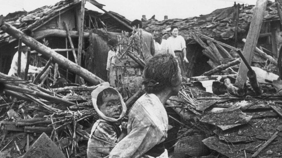 An elderly woman and her grandchild wander at their wrecked home in the aftermath of an air raid over Pyongyang, circa 1950