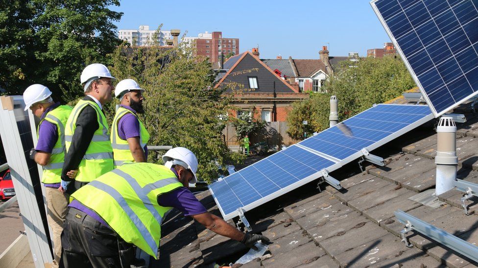 workmen installing solar panels on roof