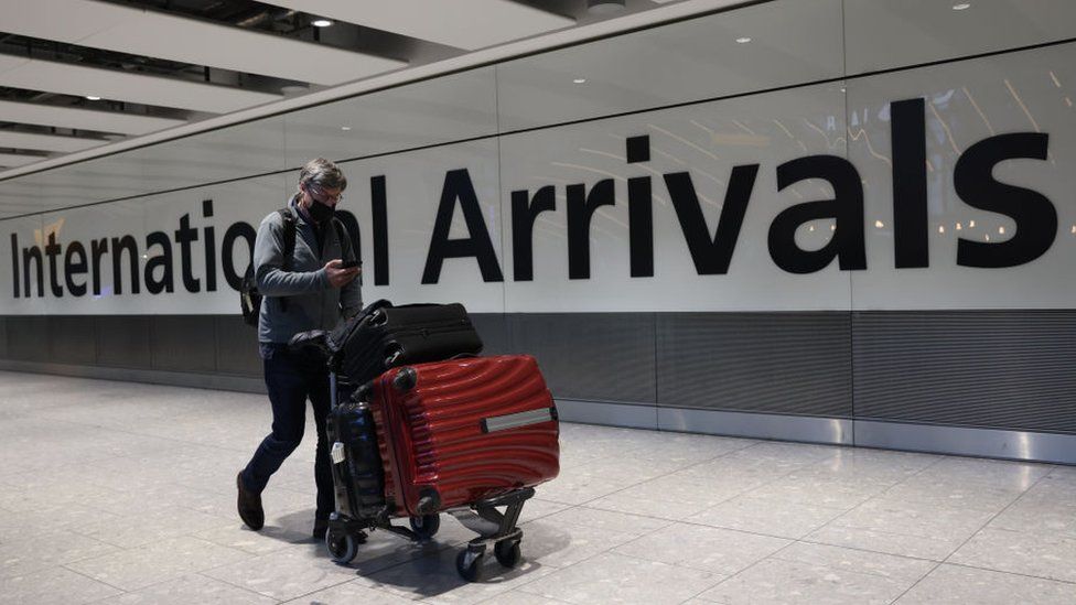 Man wearing mask with suitcases at Heathrow arrivals