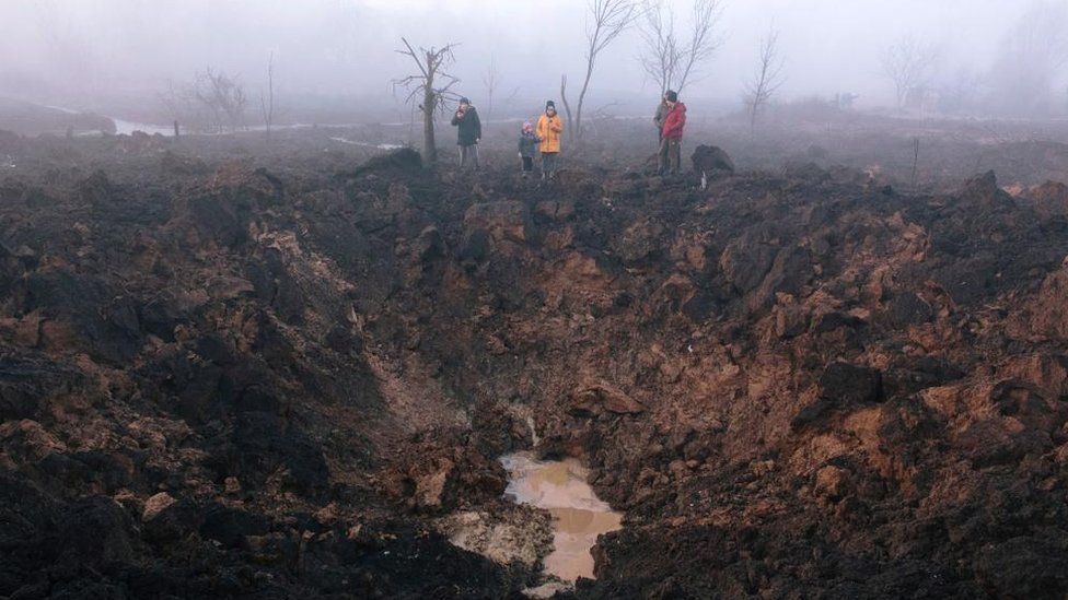 Locals gather around a shelling crater after a rocket hit the Pisochyn neighborhood outside Kharkiv
