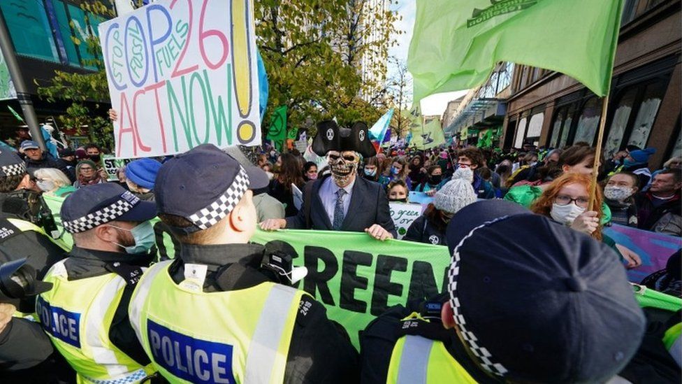Climate activists hold up banners at a protest in Glasgow, watched by police