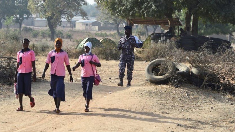 A policeman walk behind school girls as they cross the border in Yemboate, the northern Togo border post with Burkina Faso, on February 17, 2020