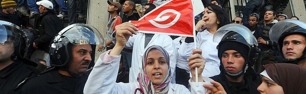 Tunisian demonstrator, holding her national country flag, is surrounded by police as she rallies in 2011