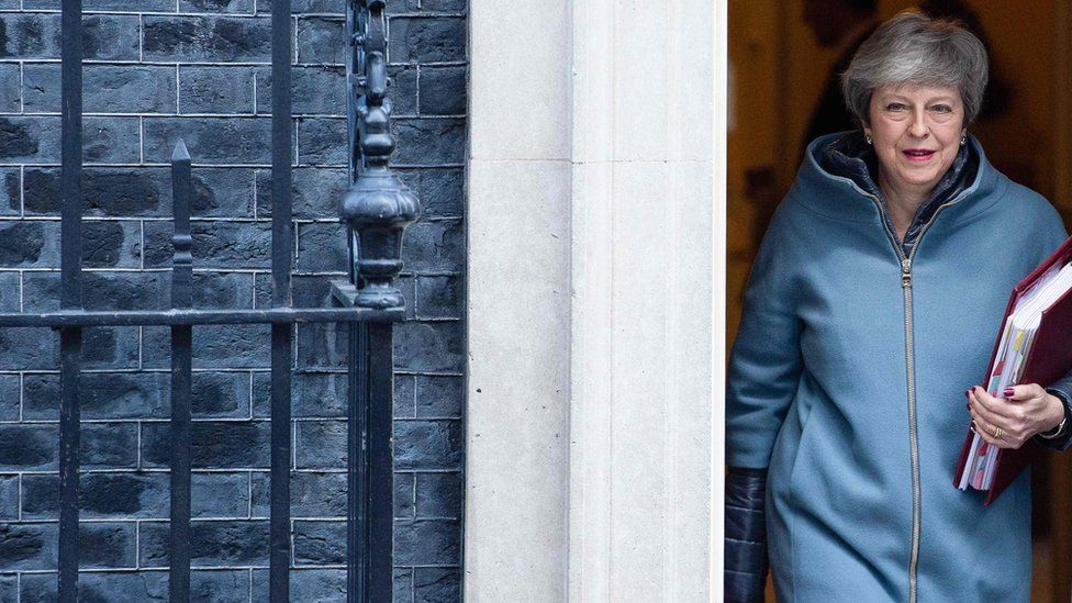 Theresa May, carrying a red folder, leaves the door of 10 Downing Street