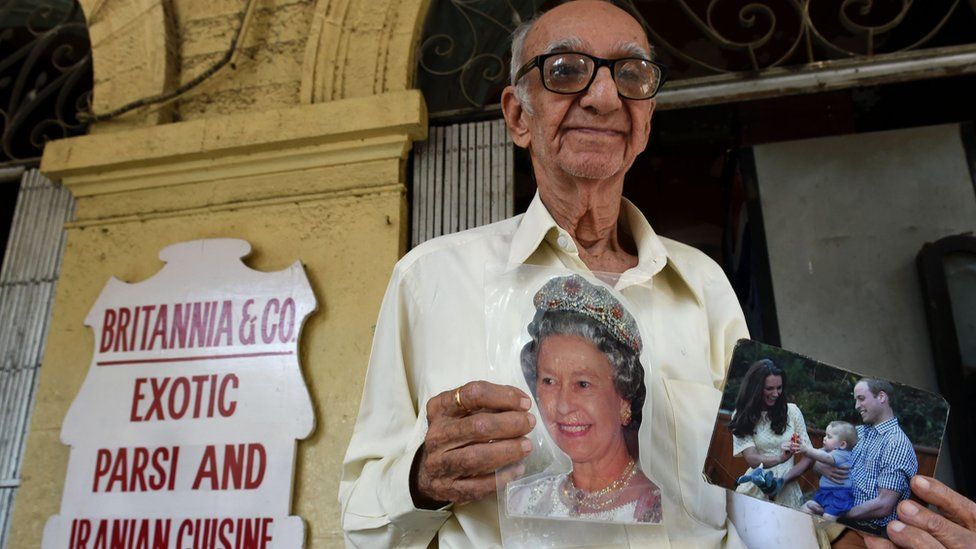 Indian restaurateur Boman Kohinoor, 93, an ardent fan of the British royal family, poses with photos of Queen Elizabeth, and the Duke and Duchess of Cambridge outside the Britannia & Co. restaurant in Mumbai on April 8, 2016,