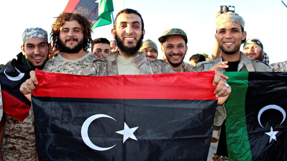 Fighters of Libyan forces allied with the U.N.-backed government hold up flags and smile
