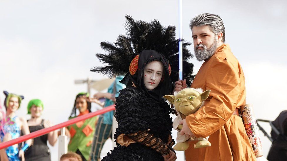 A woman dressed as Padme Amidala and a man dressed as Luke Skywalker holding a Yoda toy