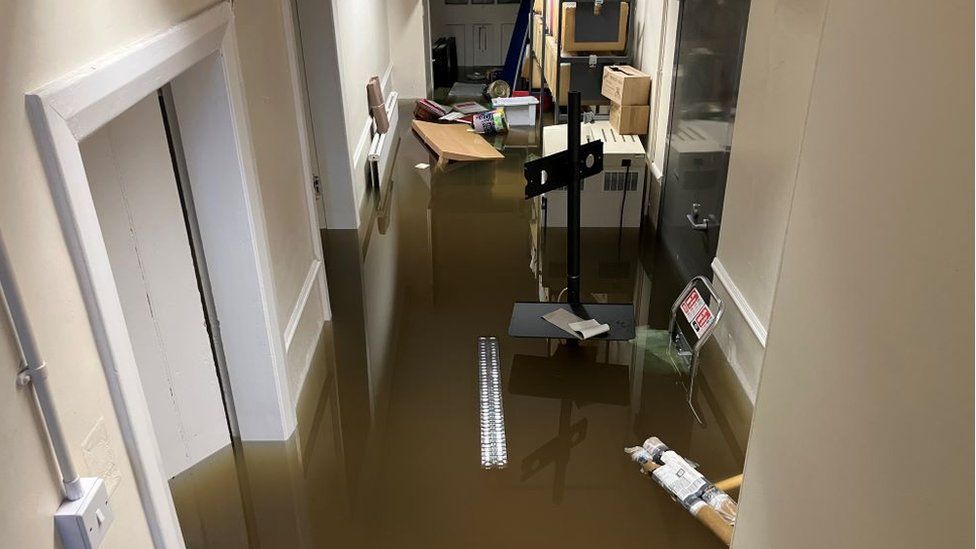 Office furniture and boxes floating in water, photographed from the stairs