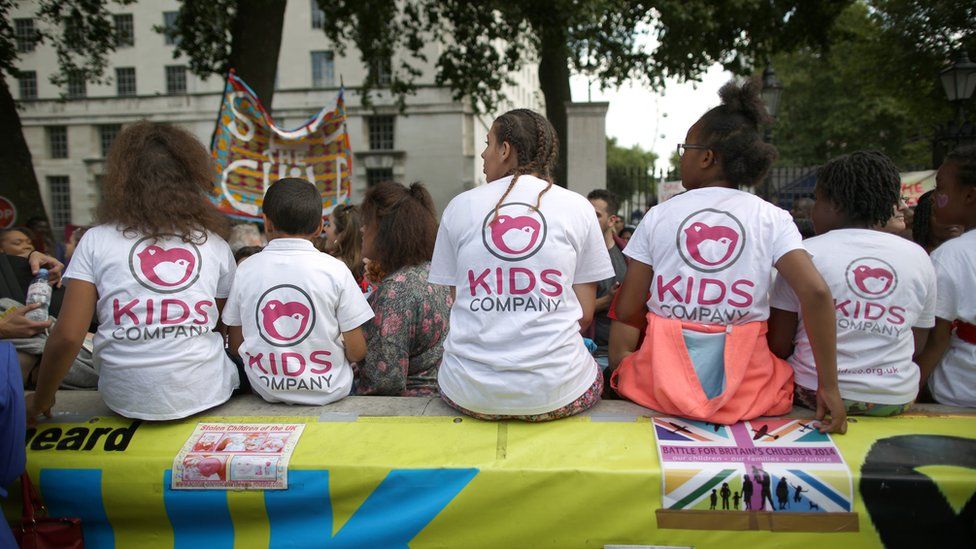 Staff members from the Kids Company charity sit on a wall with children during a rally near Downing Street on August 7, 2015 in London