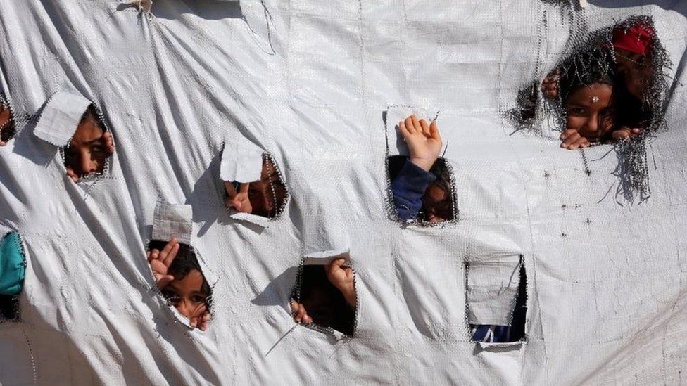 Children peer through holes in tent in al-Hawl camp