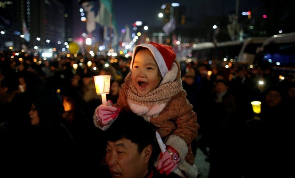 A child sitting on his father's shoulder holds a candlelight during a protest demanding South Korean President Park Geun-hye's resignation in Seoul, South Korea, on 24 December, 2016