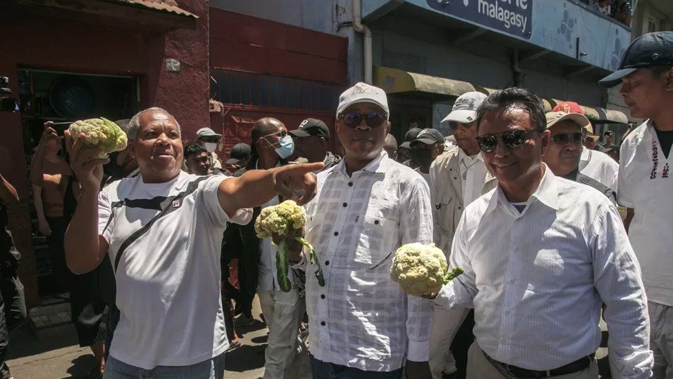 Three men, with former president Marc Ravalomanana, far right, holding cauliflowers, surrounded by protesters