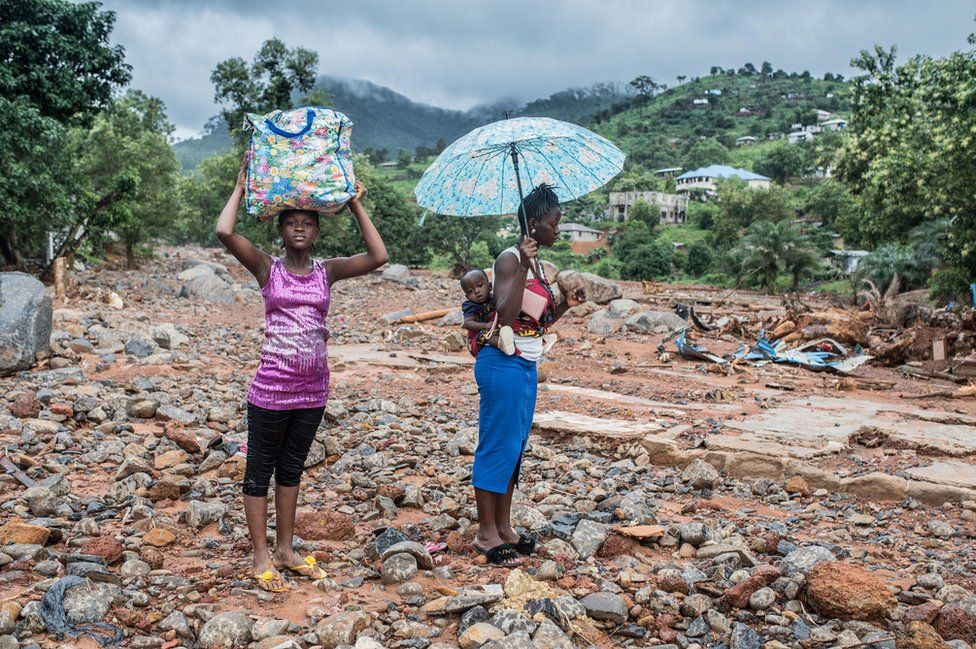 Women stand on the spot where their home once stood