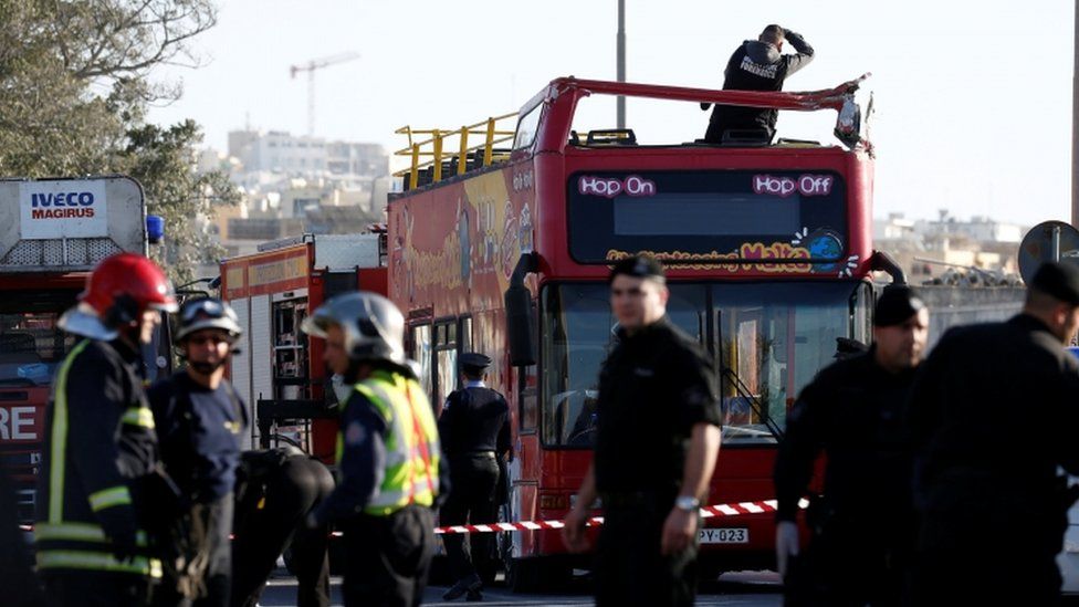 A forensics investigator stands on an open top, double-decker sightseeing bus in Zurrieq