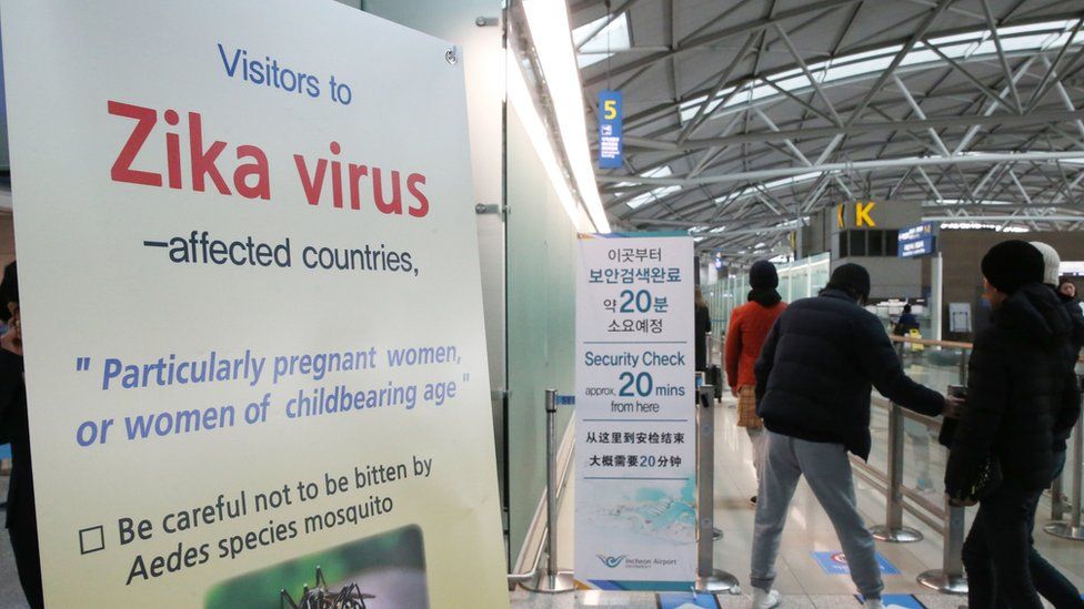 Passengers walk by a signboard about Zika virus at the passenger terminal of Incheon International Airport in Incheon, South Korea, Tuesday, March 22, 2016.